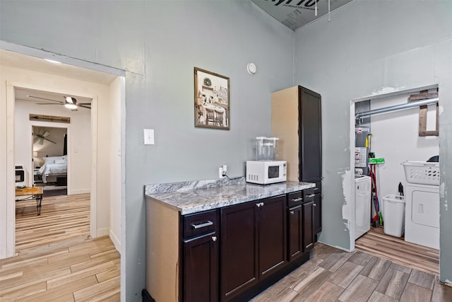 kitchen with washer and dryer, dark brown cabinetry, ceiling fan, and light stone countertops