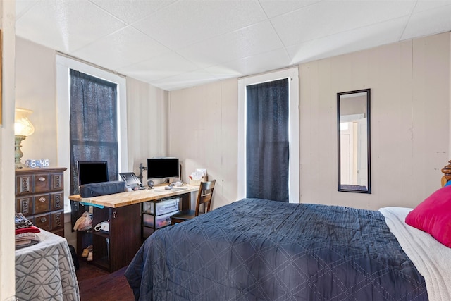 bedroom with a paneled ceiling, wooden walls, and hardwood / wood-style flooring