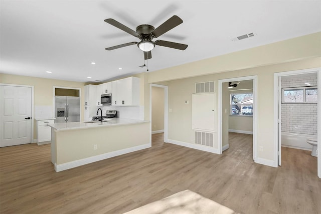 kitchen with sink, kitchen peninsula, stainless steel appliances, light hardwood / wood-style floors, and white cabinets