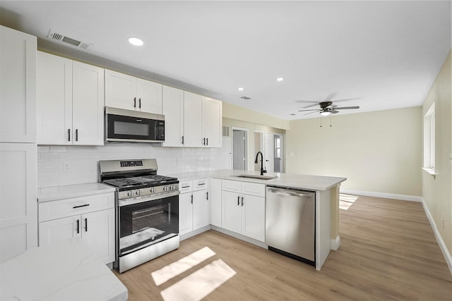 kitchen with sink, appliances with stainless steel finishes, white cabinetry, backsplash, and kitchen peninsula