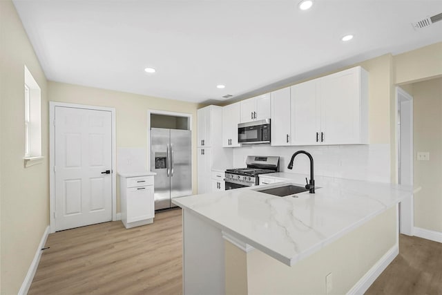 kitchen featuring sink, white cabinetry, kitchen peninsula, stainless steel appliances, and light stone countertops