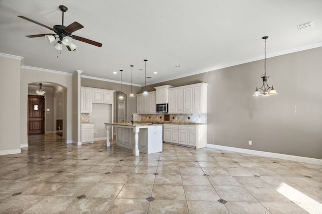 kitchen featuring a kitchen island with sink, decorative backsplash, decorative light fixtures, a kitchen bar, and white cabinetry