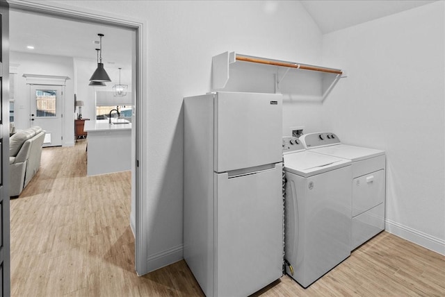 laundry area featuring baseboards, light wood finished floors, laundry area, a sink, and washing machine and dryer