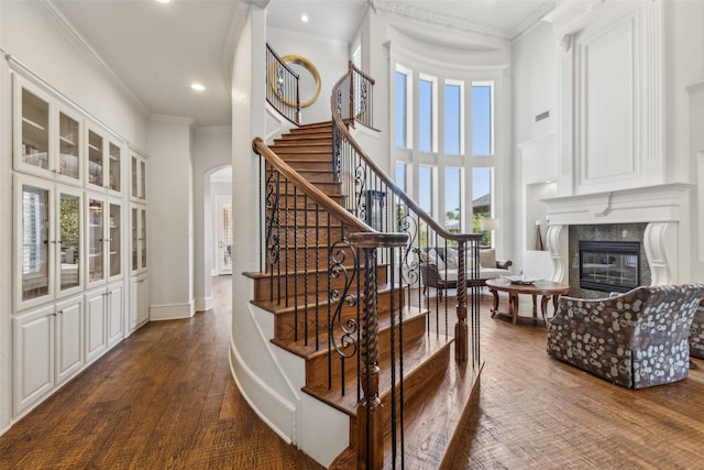 staircase featuring hardwood / wood-style floors, a premium fireplace, crown molding, and a high ceiling