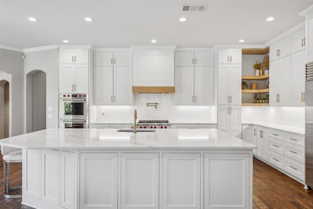 kitchen with white cabinets, a center island with sink, light stone countertops, and crown molding