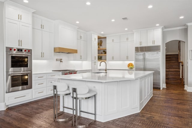 kitchen with stainless steel appliances, crown molding, dark wood-type flooring, white cabinetry, and an island with sink