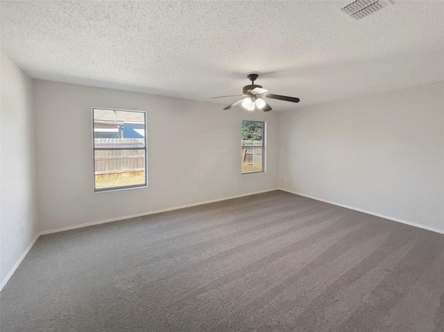 unfurnished room featuring a healthy amount of sunlight, a textured ceiling, and dark colored carpet