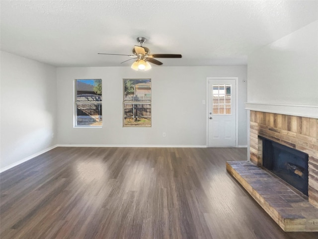 unfurnished living room featuring a textured ceiling, ceiling fan, dark hardwood / wood-style floors, and a brick fireplace