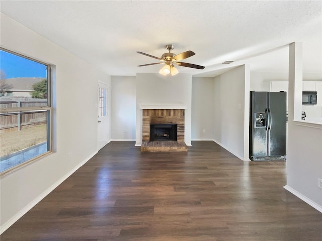 unfurnished living room featuring ceiling fan, dark hardwood / wood-style floors, a textured ceiling, and a brick fireplace