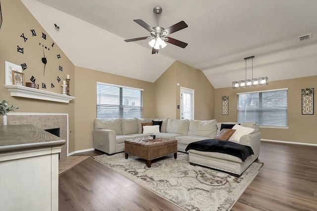 living room featuring hardwood / wood-style floors, ceiling fan, a tiled fireplace, and vaulted ceiling