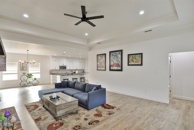 living room with ceiling fan with notable chandelier, light hardwood / wood-style floors, a raised ceiling, and crown molding