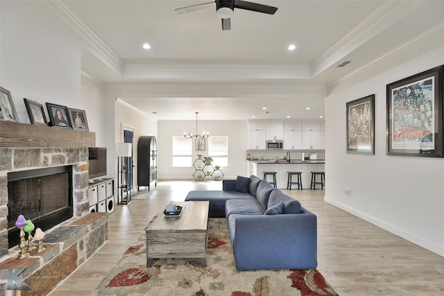 living room with a fireplace, a raised ceiling, ceiling fan with notable chandelier, and light hardwood / wood-style flooring