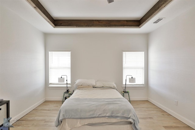 bedroom featuring a raised ceiling, multiple windows, and light wood-type flooring