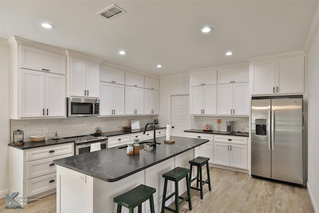 kitchen featuring light wood-type flooring, stainless steel appliances, sink, white cabinetry, and an island with sink