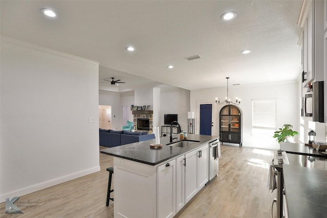 kitchen with a center island with sink, ceiling fan with notable chandelier, white cabinets, a stone fireplace, and sink