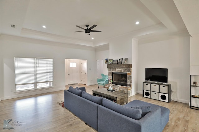 living room with ceiling fan, light hardwood / wood-style floors, a raised ceiling, and a stone fireplace