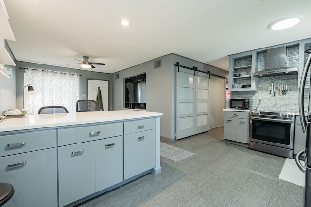 kitchen featuring stainless steel range with electric stovetop, backsplash, wall chimney range hood, ceiling fan, and a barn door