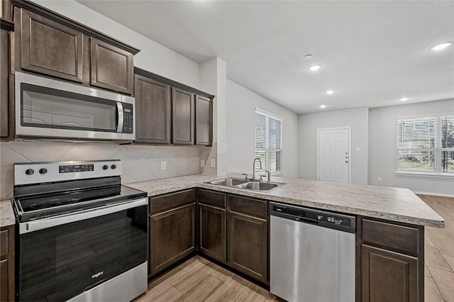 kitchen featuring kitchen peninsula, appliances with stainless steel finishes, backsplash, dark brown cabinetry, and sink