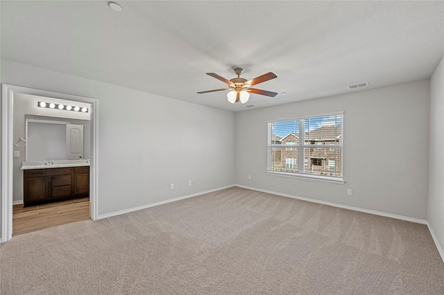 unfurnished bedroom with ceiling fan, sink, light carpet, and ensuite bath