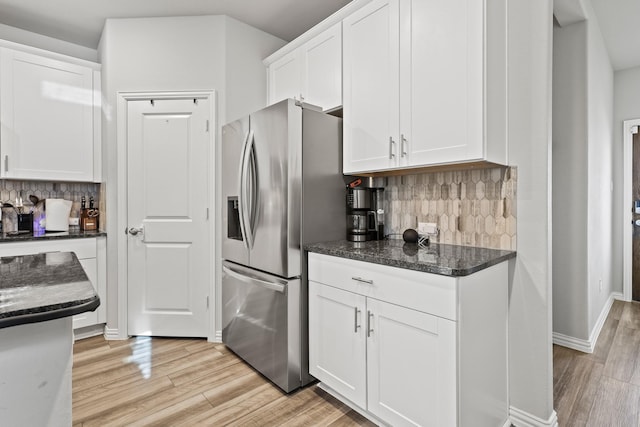 kitchen with white cabinets, stainless steel refrigerator with ice dispenser, backsplash, and dark stone counters