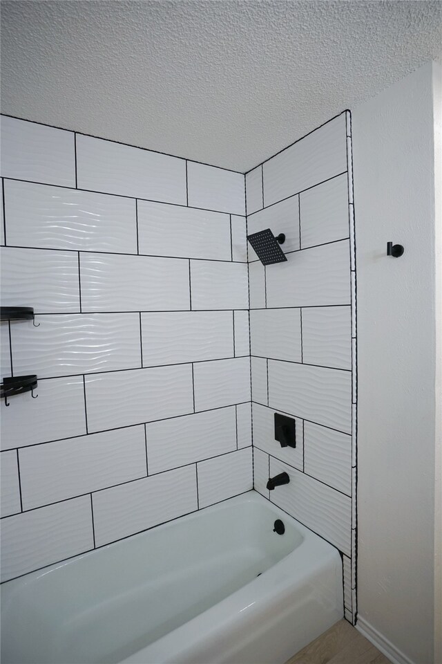 bathroom with a textured ceiling and tiled shower / bath