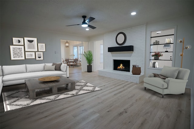 living room with a brick fireplace, ceiling fan, a textured ceiling, and light hardwood / wood-style flooring