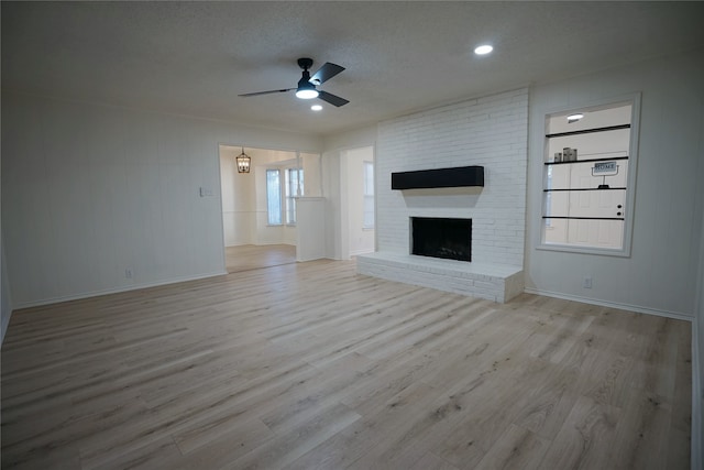 unfurnished living room with ceiling fan, a fireplace, and light wood-type flooring