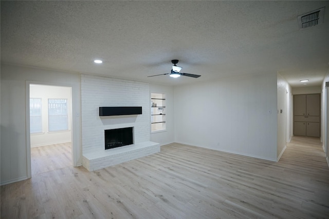 unfurnished living room with a textured ceiling, ceiling fan, a fireplace, and light hardwood / wood-style flooring