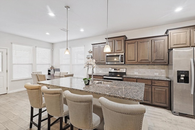 kitchen featuring sink, a kitchen island with sink, pendant lighting, stainless steel appliances, and light hardwood / wood-style floors