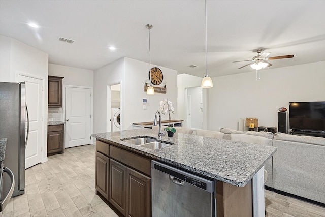 kitchen featuring pendant lighting, sink, appliances with stainless steel finishes, a center island with sink, and washer / clothes dryer