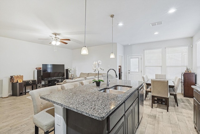 kitchen featuring dishwasher, an island with sink, sink, hanging light fixtures, and light hardwood / wood-style flooring