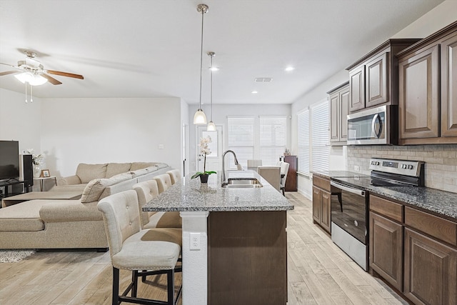 kitchen featuring sink, hanging light fixtures, a center island with sink, appliances with stainless steel finishes, and a kitchen breakfast bar