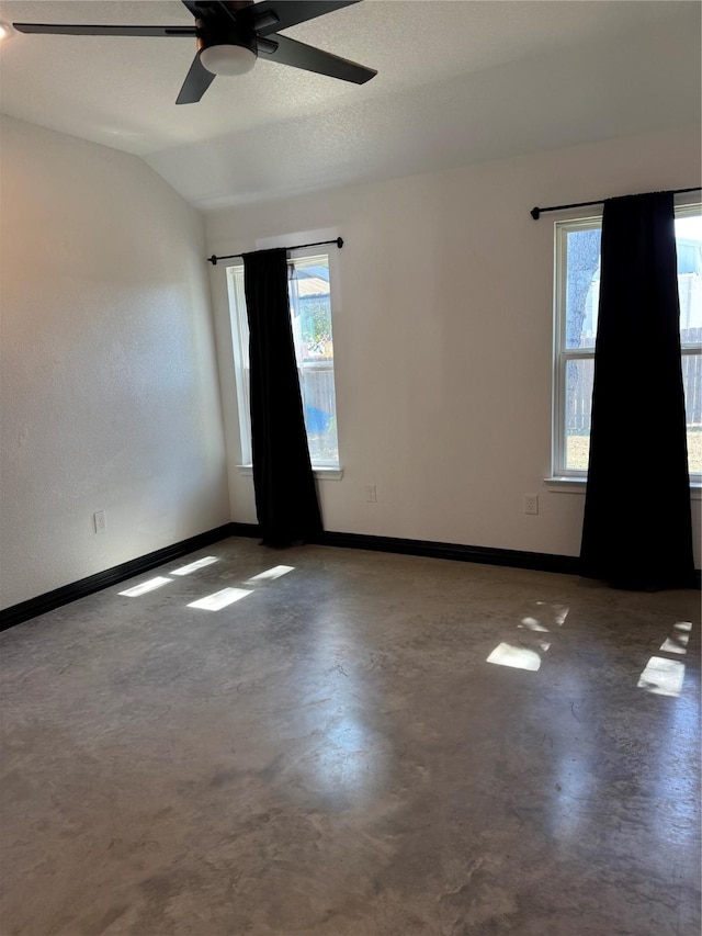 empty room featuring ceiling fan, plenty of natural light, concrete floors, and vaulted ceiling