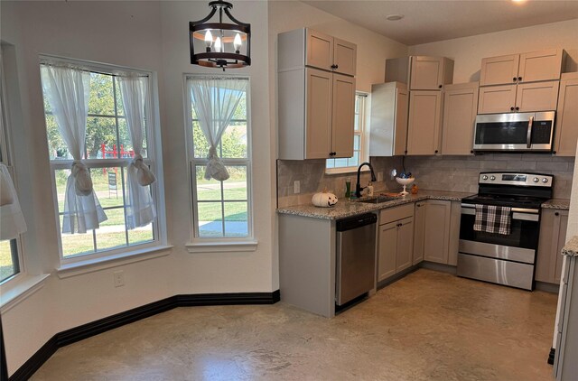 kitchen with backsplash, sink, light stone countertops, appliances with stainless steel finishes, and decorative light fixtures