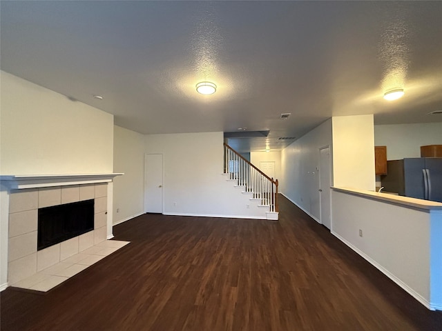 unfurnished living room featuring dark hardwood / wood-style flooring, a textured ceiling, and a tiled fireplace