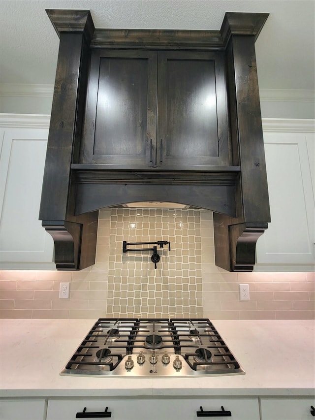 kitchen featuring white cabinets, stainless steel gas stovetop, decorative backsplash, and ornamental molding