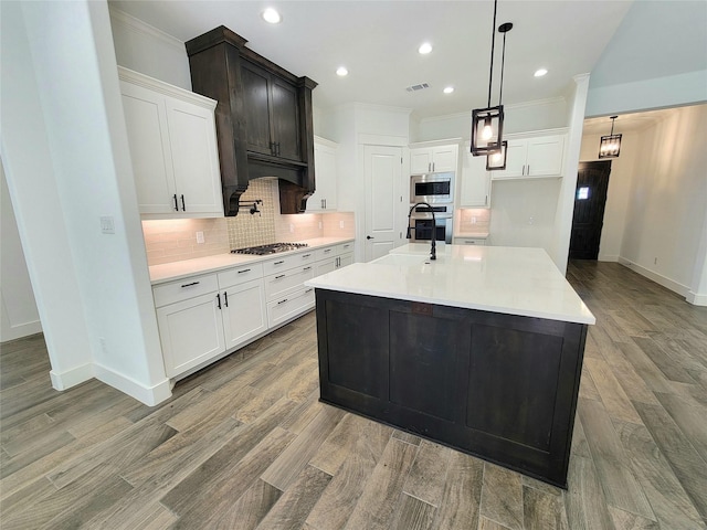 kitchen with stainless steel appliances, white cabinetry, and an island with sink