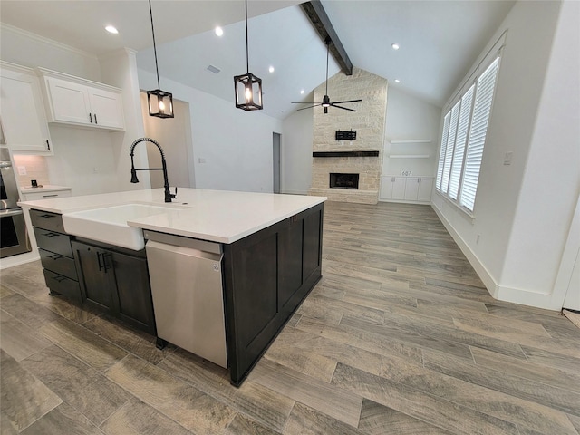 kitchen with appliances with stainless steel finishes, a kitchen island with sink, sink, white cabinetry, and a stone fireplace