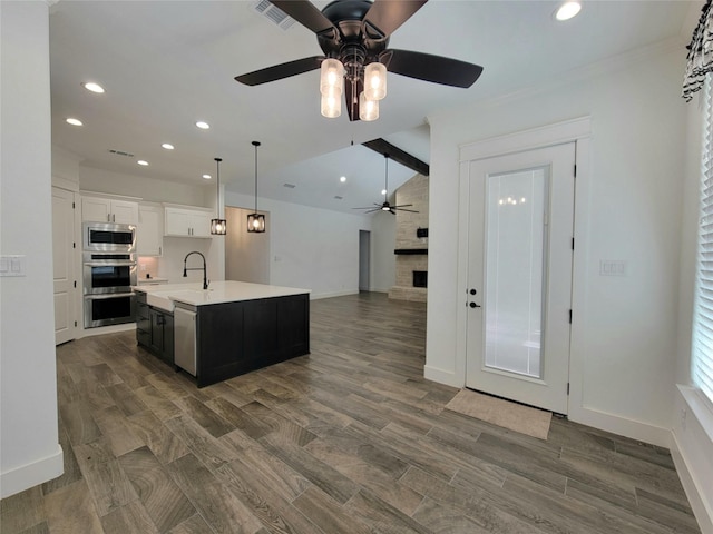 kitchen with a kitchen island with sink, white cabinets, lofted ceiling with beams, ceiling fan, and appliances with stainless steel finishes