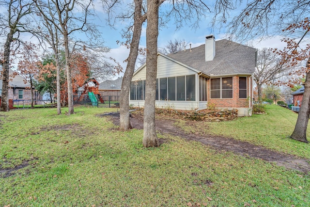 rear view of property with a yard, a playground, and a sunroom