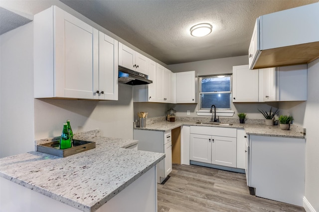 kitchen with sink, kitchen peninsula, light hardwood / wood-style floors, a textured ceiling, and white cabinets