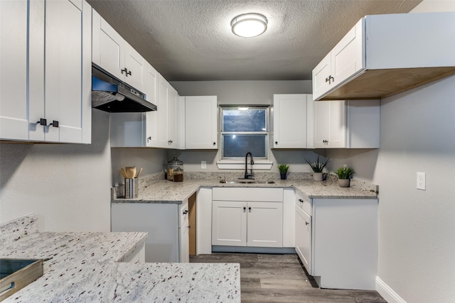 kitchen featuring white cabinets, sink, light hardwood / wood-style flooring, light stone countertops, and a textured ceiling