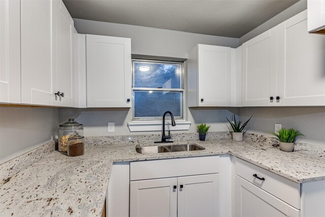 kitchen with light stone countertops, white cabinetry, and sink