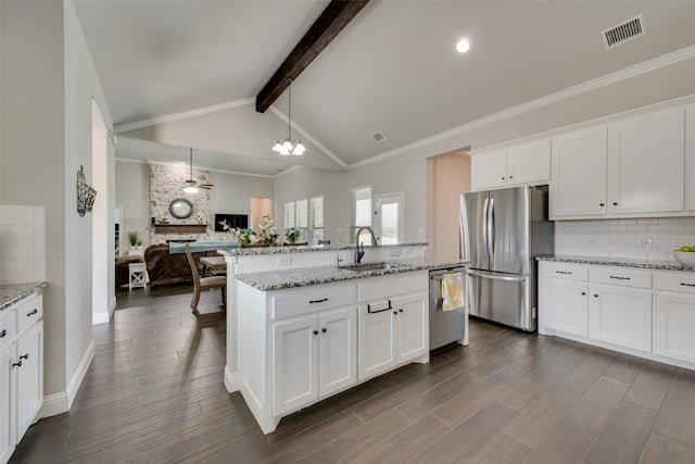 kitchen featuring sink, vaulted ceiling with beams, appliances with stainless steel finishes, pendant lighting, and white cabinets