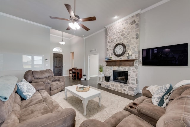 living room featuring dark wood-type flooring, ornamental molding, ceiling fan, a fireplace, and a high ceiling