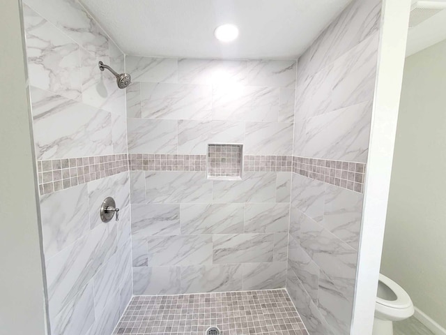 bathroom with a tile shower and toilet