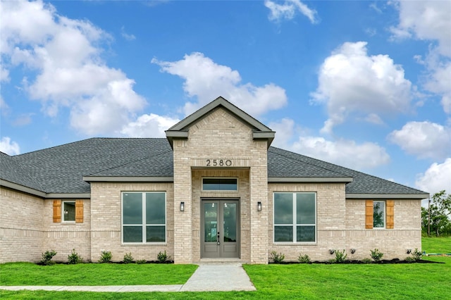 view of front facade with french doors, a front yard, roof with shingles, and brick siding