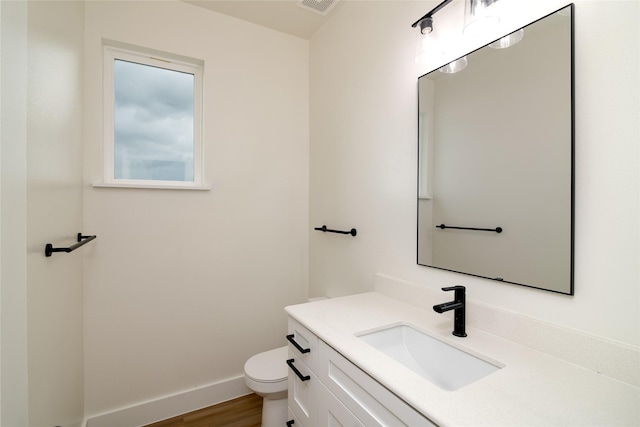 bathroom with toilet, visible vents, baseboards, wood finished floors, and vanity