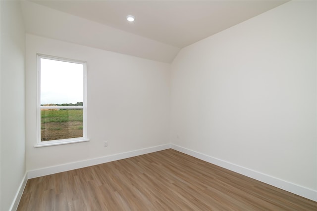 spare room featuring wood-type flooring and vaulted ceiling