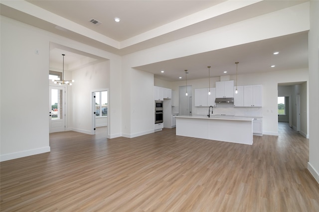 unfurnished living room featuring sink, light hardwood / wood-style floors, and a chandelier